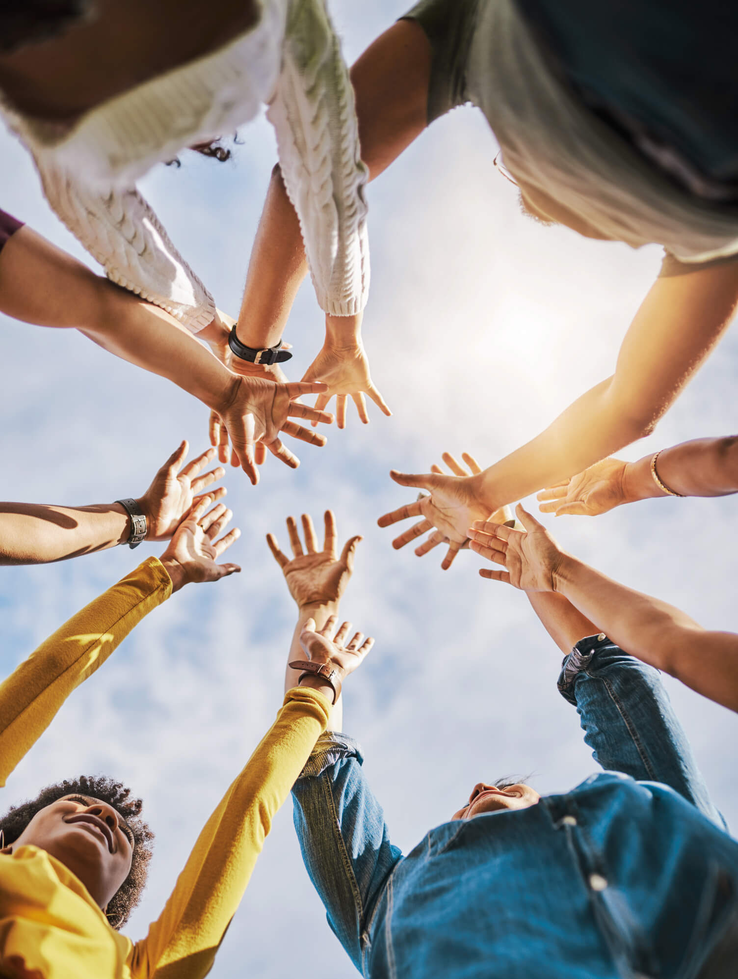 Diverse group of individuals joining hands in unity, viewed from below